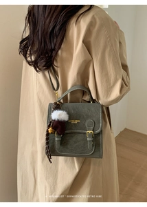 Detail eines dunkelgrünen Lederrucksacks mit Vintage-Bronzebeschlägen und Bärenanhänger