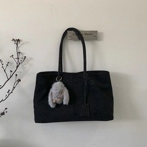 Detail of black matte tote bag hanging with a cute plush charm and long shoulder straps