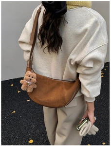 Close-up of brown suede crescent bag featuring a cute plush bear pendant on long strap
