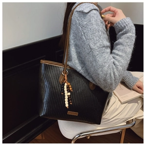 Detail of woven texture tote bag with wooden bead tassel and brown shoulder straps