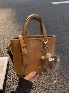 Vintage brown leather tote bag with gold logo and plush charm on an urban street background