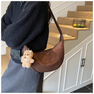 Detailed side view of a brown suede hobo bag with a plush bear charm on a model