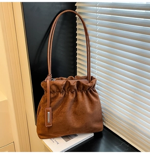 Detailed view of brown faux suede bucket bag with pleats and thin straps on a windowsill