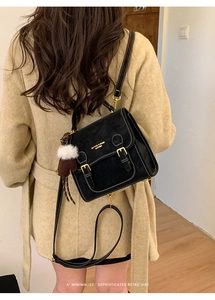 Schwarze Vintage-Umhängetasche mit Goldschnallen und Herz-Anhänger an beige Mantel