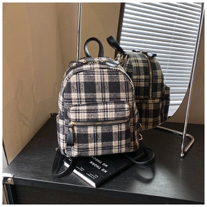 Close-up of black and white plaid tweed backpack with gold zipper and leather strap
