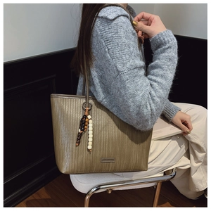 Close-up of a khaki woven tote bag featuring a beaded tassel and metal logo detail