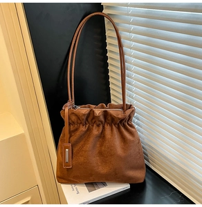 Detail view of brown suede bucket bag featuring pleated design and thin shoulder strap
