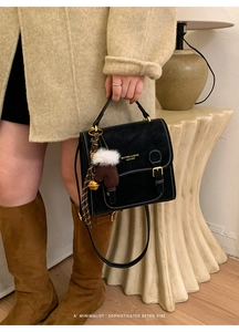 Detail einer schwarzen Wildledertasche mit Goldbeschlägen und Plüschhandschuh-Anhänger