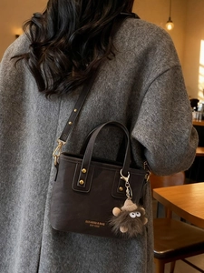 Retro dark brown crossbody bucket bag with plush monster charm shown in a cozy cafe setting