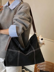 Grand sac hobo noir avec surpiqûres contrastées et bandoulière en cuir marron sur modèle