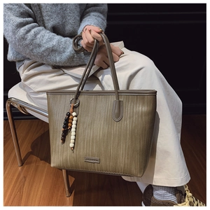 Detail of a brown woven tote bag featuring a beaded pendant and metal logo on the surface