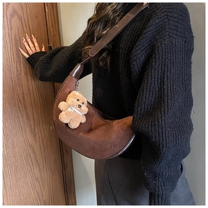 Detail of a brown suede crescent bag featuring an adjustable strap and a plush bear charm