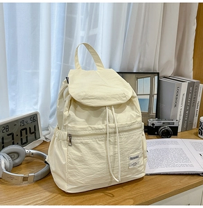 Détail d'un sac à dos en nylon crème avec cordon de serrage, poche zippée et étiquette tissée