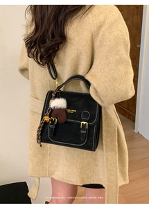 Detail der schwarzen Retro-Handtasche mit weißen Kontrastnähten und weichem Plüsch-Anhänger