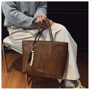 Close-up of brown woven tote bag with colorful bead charm and leather brand tag
