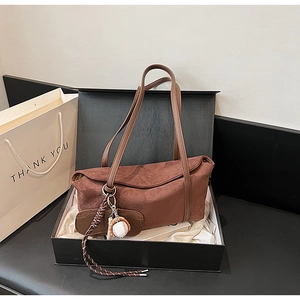 Detail of a brown suede shoulder bag with a unique baseball charm in a gift box