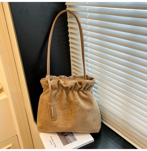 Detail of khaki suede bucket bag with drawstring closure and metal charm accessory