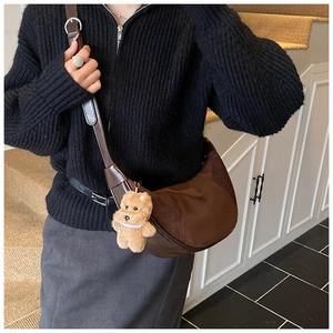 Brown suede dumpling bag with cute plush bear charm worn by a model in casual style