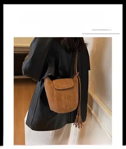 Détail du sac seau en daim marron chaud avec pompon à franges porté à l'épaule
