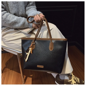 Detail of black woven tote bag with V-shaped texture, brown leather handles and brand logo