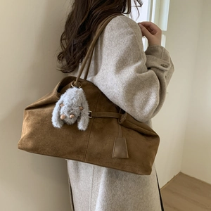 Detailed side view of large brown suede tote bag with cute plush pendant on a model