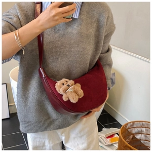 Detailed view of burgundy crescent crossbody bag with plush bear charm and mixed textures