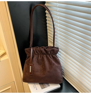Detailed close-up of dark brown suede bucket bag with drawstring and leather strap