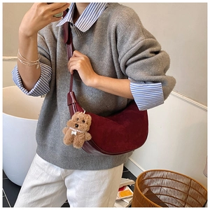 Detail of a dark red crescent shoulder bag featuring a cute plush bear charm accessory