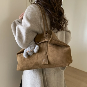 Detail of a large brown suede tote bag with a plush bear charm worn by a model