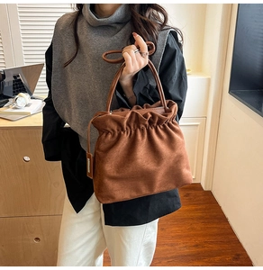 Close-up of brown suede bucket bag with drawstring closure and silver metal hardware