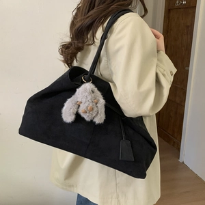 Detail of black matte tote bag with plush rabbit charm worn over a khaki trench coat