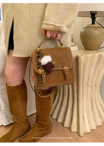 Detail der braunen Vintage-Lederhandtasche mit Doppelschnallen und Plüschhandschuh-Anhänger