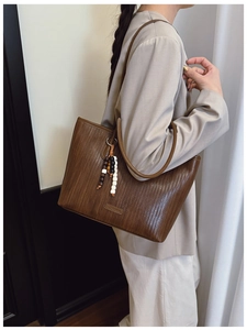 Brown tote bag with woven texture and beaded tassel accessory on female model