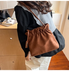 Brown suede bucket bag detail showing drawstring closure and elegant metal charm pendant