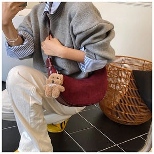 Detail view of burgundy suede crescent bag with a small brown teddy bear charm accessory