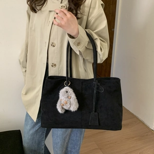 Detail of black matte tote bag with plush rabbit pendant on shoulder of beige trench coat