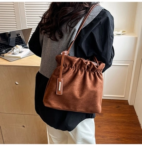 Detail of caramel brown suede bucket bag with pleated closure and silver metal pendant