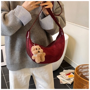 Detail of burgundy suede crescent shoulder bag with a cute plush bear charm accessory