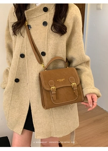 Detail einer braunen Vintage-Leder-Umhängetasche mit Metallschnallen und Tragegriff am Model