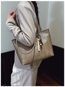 Detail of woven tote bag featuring beaded fringe and metallic brand logo accents