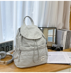 Sac à dos en nylon gris clair avec fermeture à cordon et rabat sur un bureau en bois brun