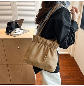Brown suede bucket bag with drawstring closure worn by a model in a cozy office setting