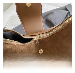Détail du sac bandoulière en daim marron montrant le zip doré et la fermeture magnétique
