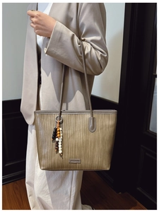 Detail of taupe woven tote bag with bohemian beaded tassel and metal logo on strap
