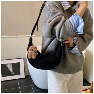 Detail of black crescent suede shoulder bag featuring a cute brown plush bear charm