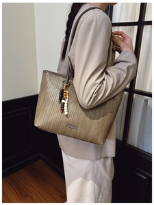 Brown woven tote bag detail featuring wooden bead tassel and minimalist metal nameplate