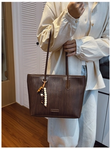 Close-up of dark brown tote bag featuring a V-shaped woven texture and wooden bead charm