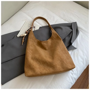 Minimalist caramel brown tote bag with woven pendant on white bedding setup