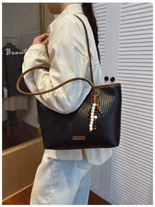 Detail of black woven tote bag with brown leather straps and colorful beaded charm