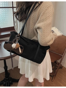 Large black canvas tote bag with baseball charm on model in cozy cafe setting